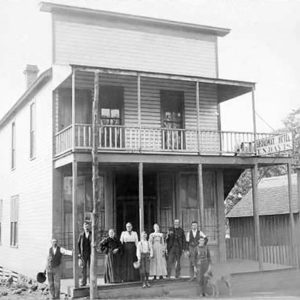 White men and women standing on porch of multistory wooden building