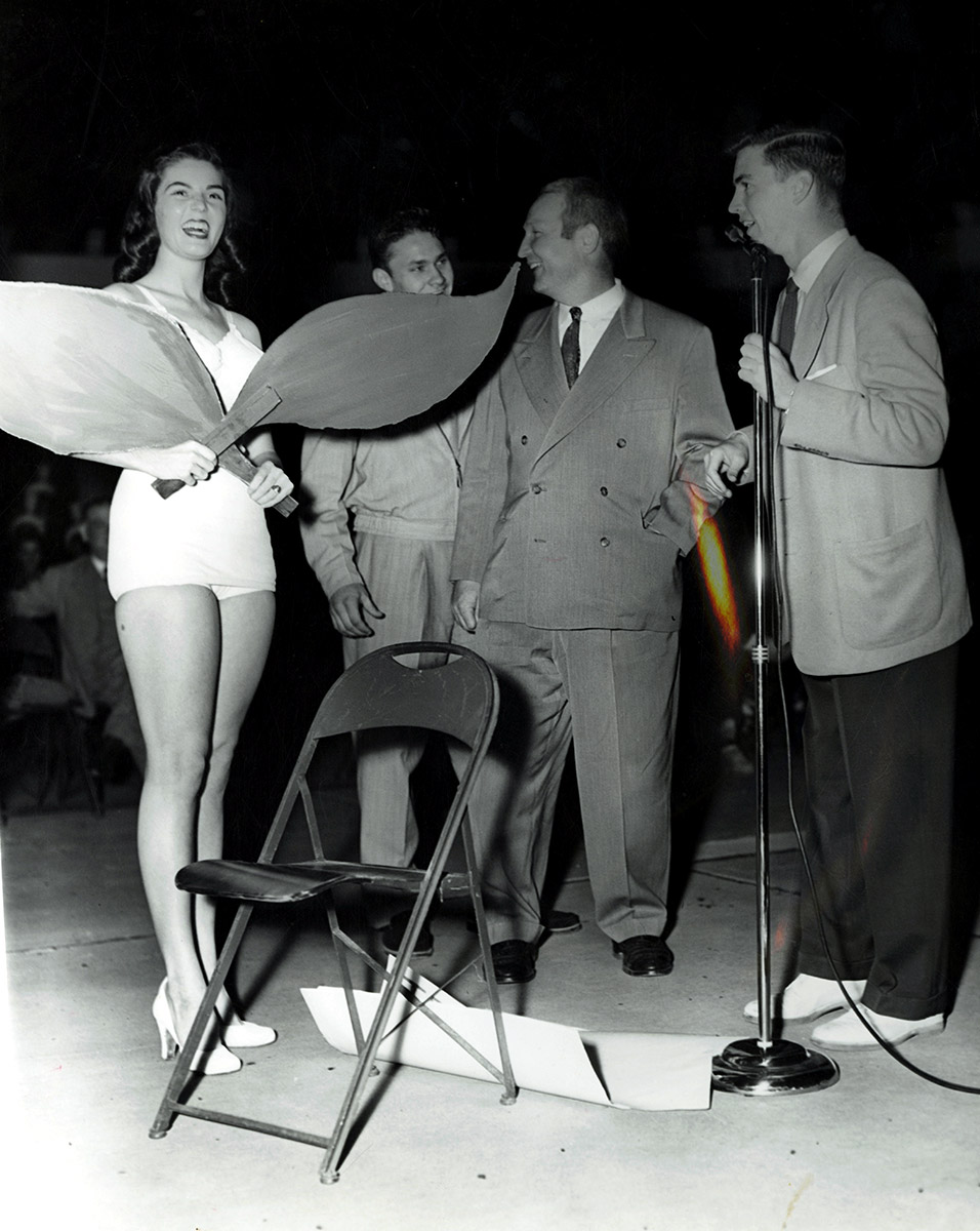 White women in bathing suit on stage with three white men in suits