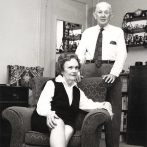 White man standing and white woman sitting in interior room