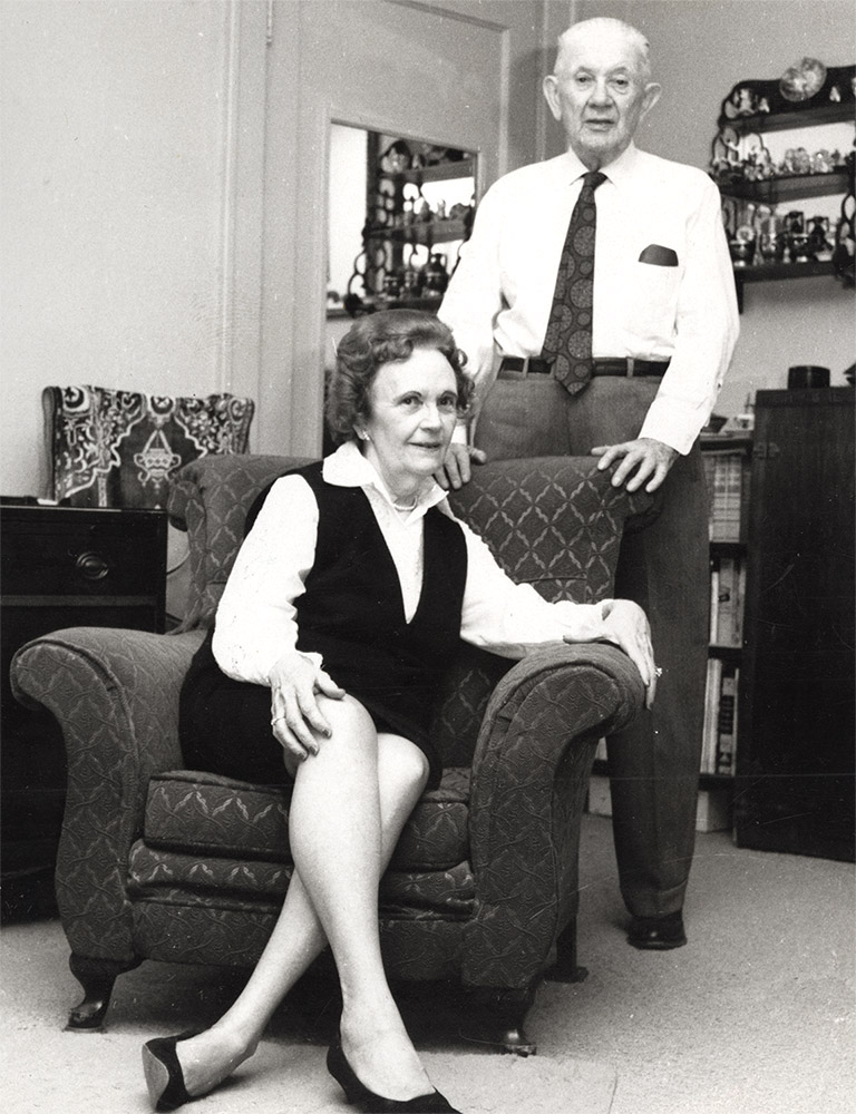 White man standing and white woman sitting in interior room