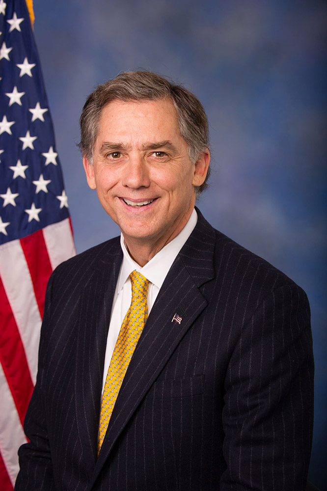 White man in suit and tie in front of American flag