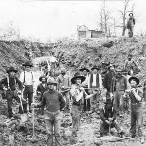 Group of men with picks and shovels working in ditch