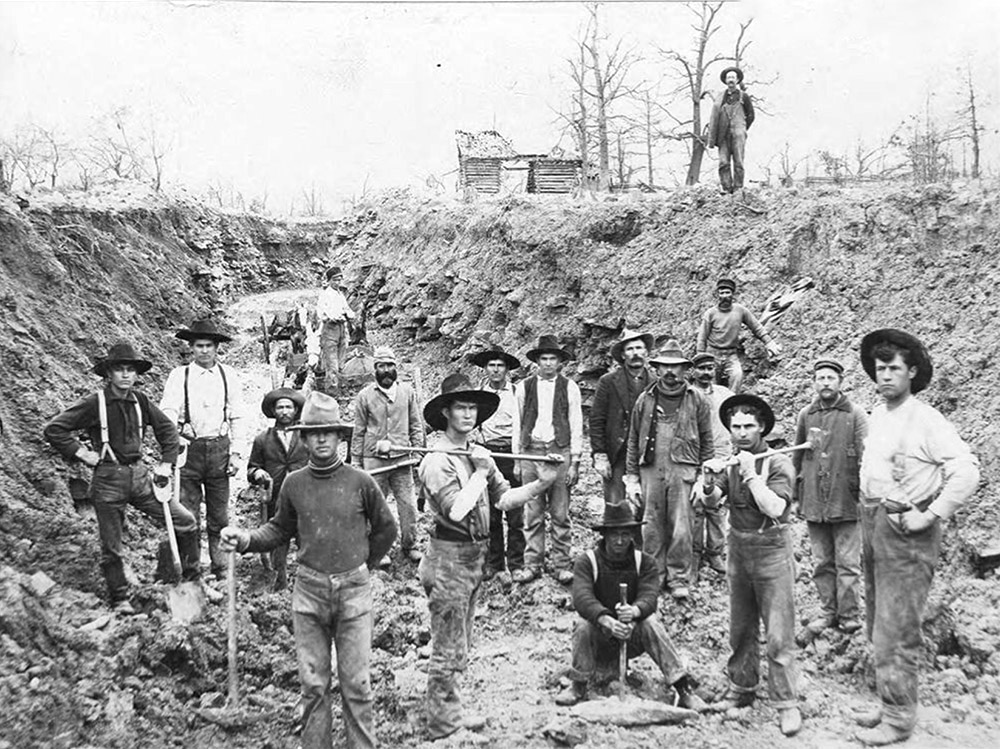 Group of men with picks and shovels working in ditch