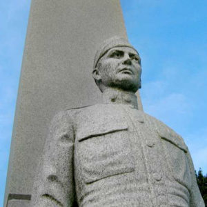 Gray granite statue of serious-faced man in military uniform in front of tall monument