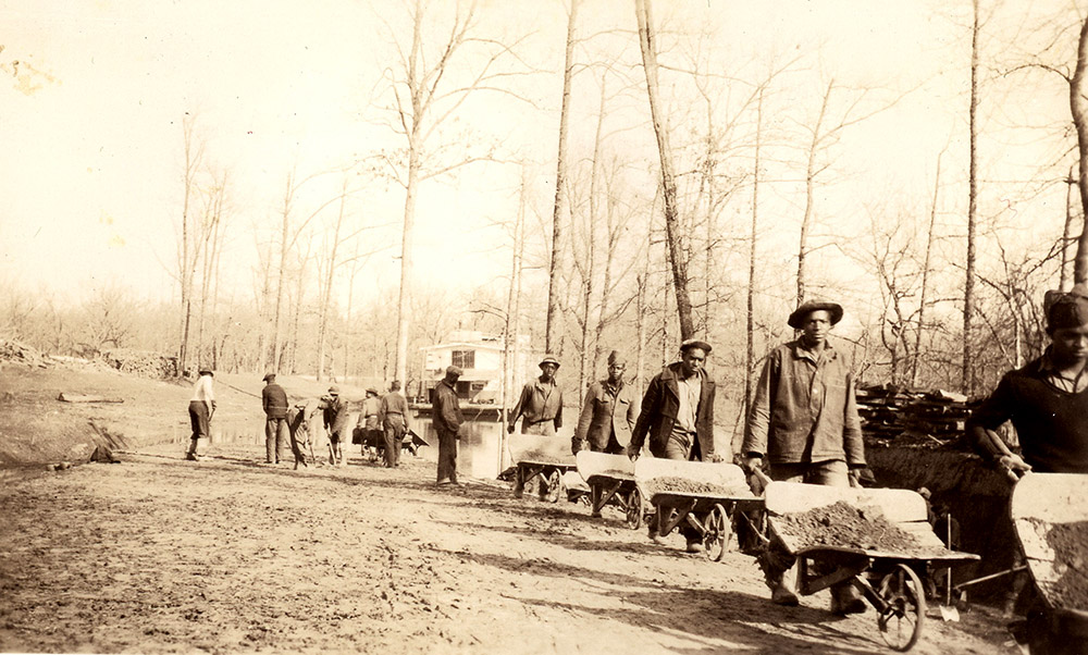 Row of African American men pushing wheelbarrows along dirt path