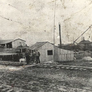 Men standing on railroad tracks in front of several wooden buildings