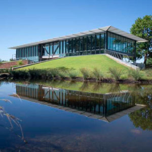 Single story glass building on shore of pond with reflection showing on water