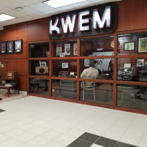 items behind glass and a sitting area with radio displayed under a sign saying KWEM