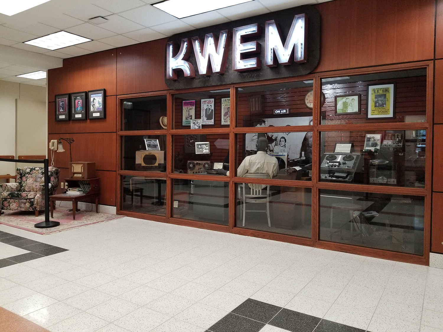 items behind glass and a sitting area with radio displayed under a sign saying KWEM