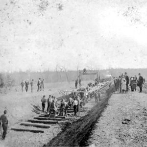 Large group of men working on laying railroad tracks with spectators on both sides
