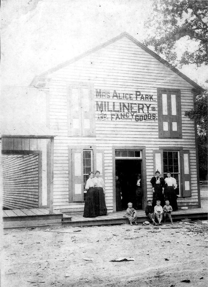 Multistory wooden building with white women standing before it and children sitting on the front step