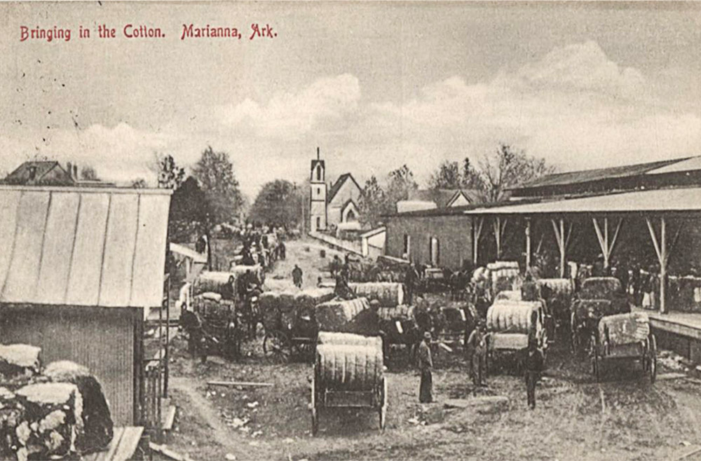 Wagons loaded down with bales filling a dirt road running through a downtown area