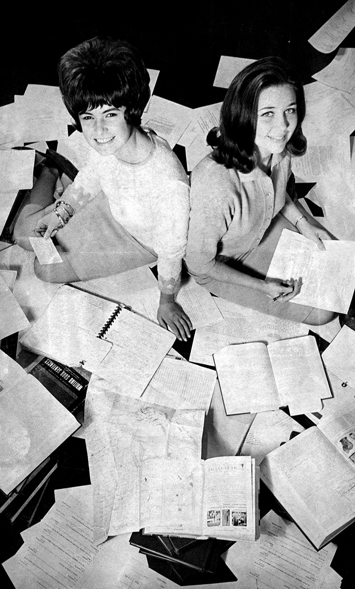 Two white women seated amid papers and books