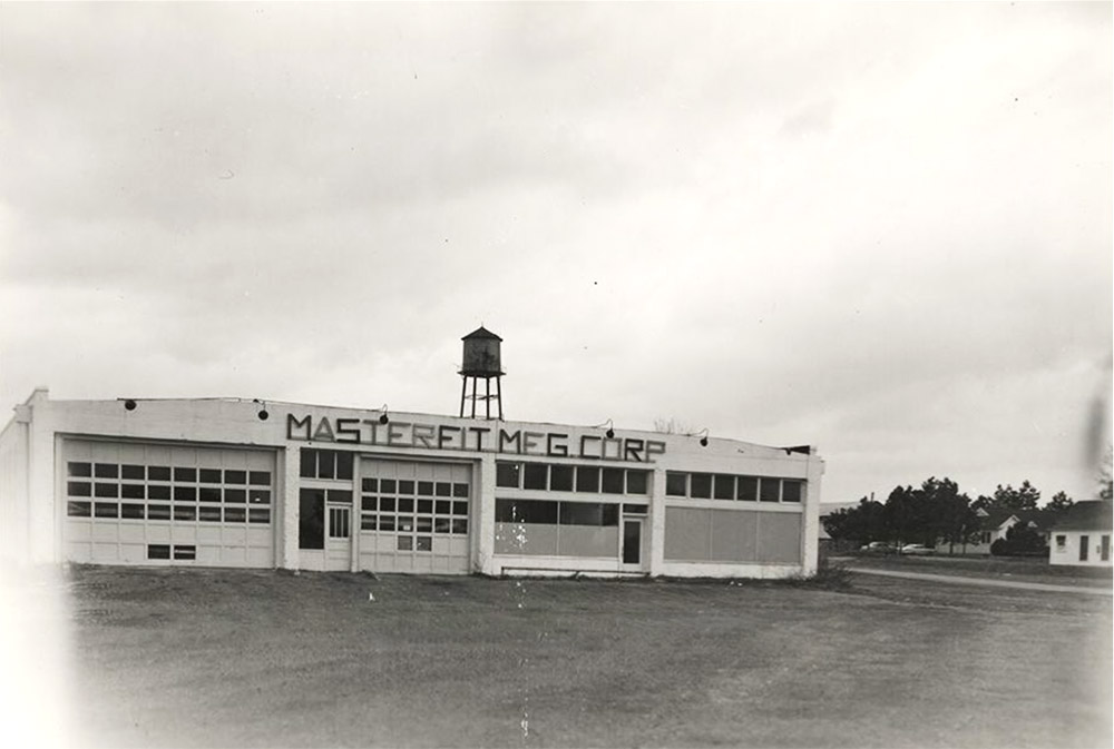 Single story white concrete block building with water tank on top with "Masterfit Manufacturing Corporation" on the front