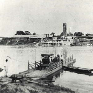 Horse and buggy on ferry; town visible across river