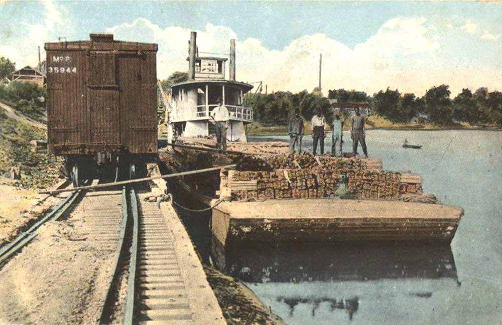 Men standing on barge in front of steamboat beside railroad tracks and train
