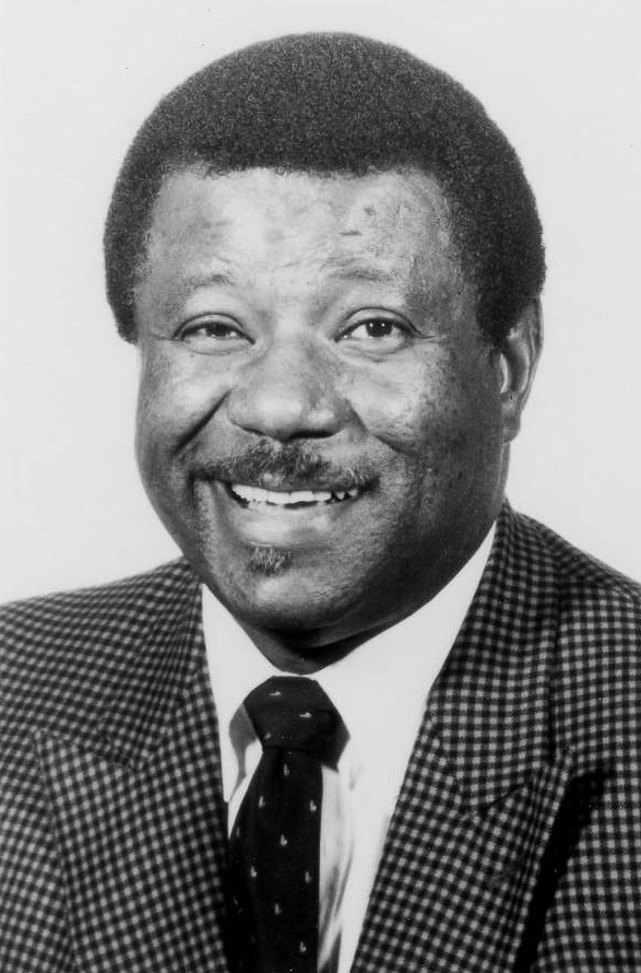 smiling mustachioed African American man in checkered sports jacket and dark tie