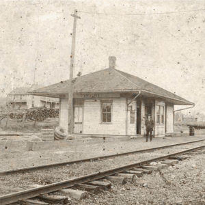 Single story building next to railroad tracks with man standing in front
