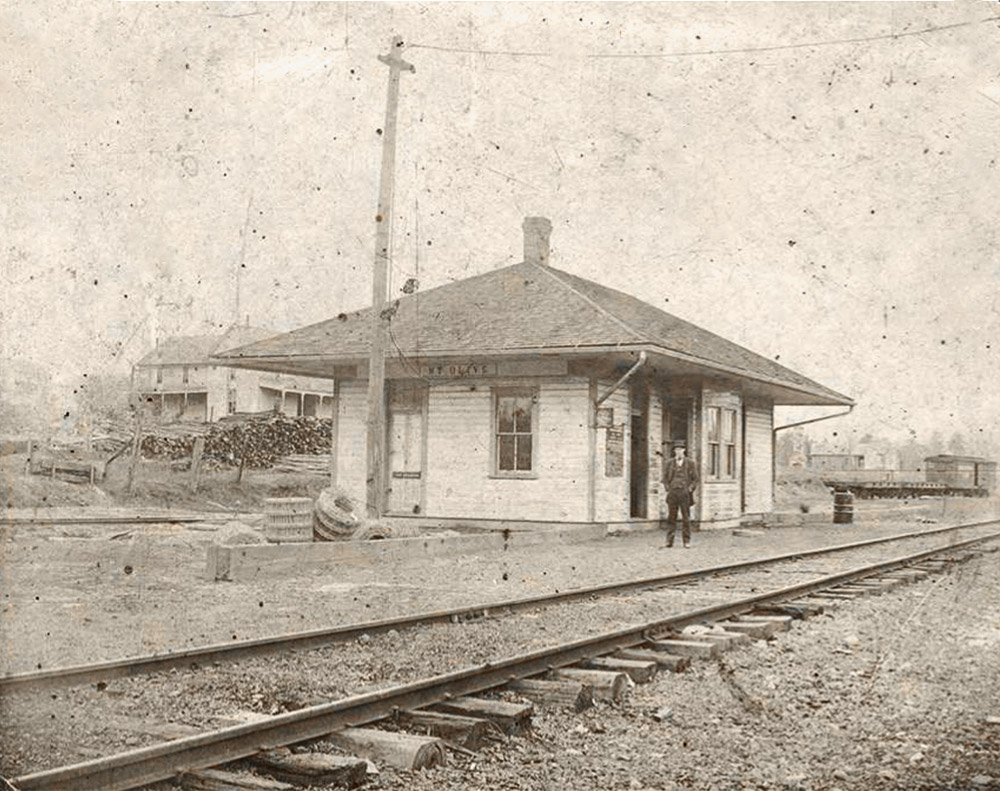Single story building next to railroad tracks with man standing in front