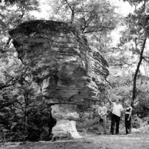 People looking at top-heavy rock formation
