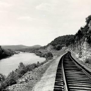 Railroad tracks running beside river with rock face on right side