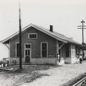 Single story wooden building alongside railroad tracks