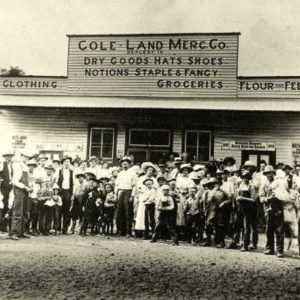Large group of people standing in front of wooden building "Cole Land Mercantile"