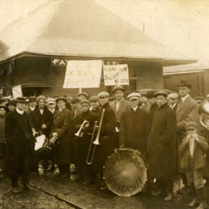 Crowd of people carrying signs and musical instruments in front of single story building