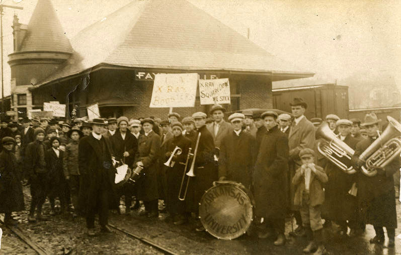 Crowd of people carrying signs and musical instruments in front of single story building