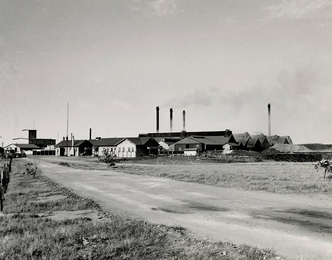 Factory buildings with smoke stacks emitting smoke and road in the foreground