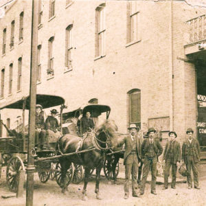 People standing with wagon before multistory brick building