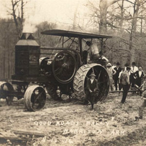 Large group of white men standing around tractor and other mechanical implements