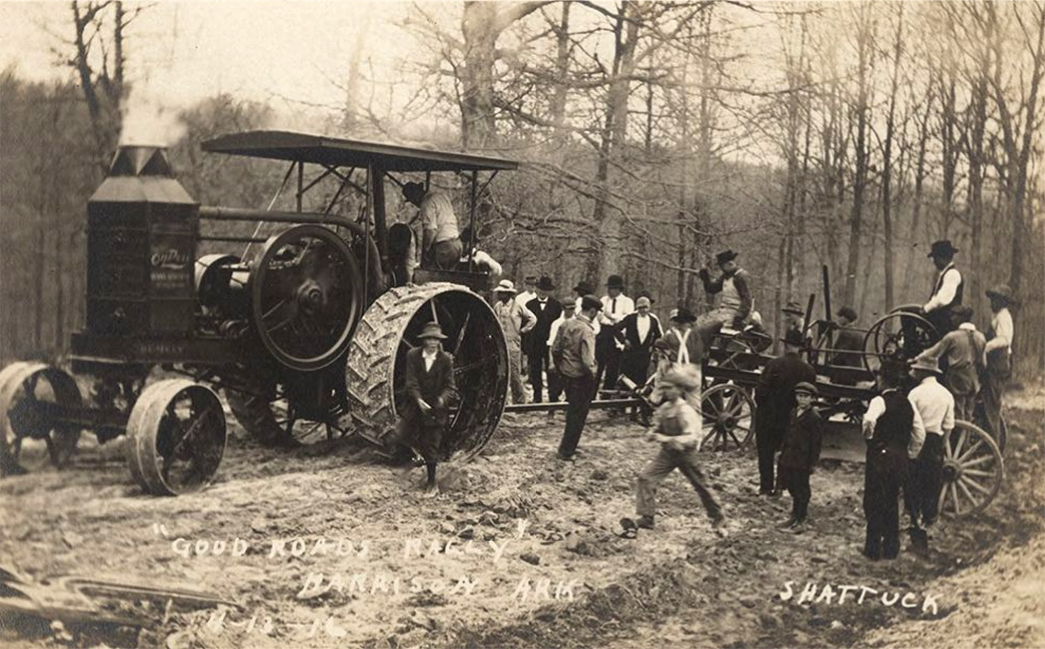 Large group of white men standing around tractor and other mechanical implements