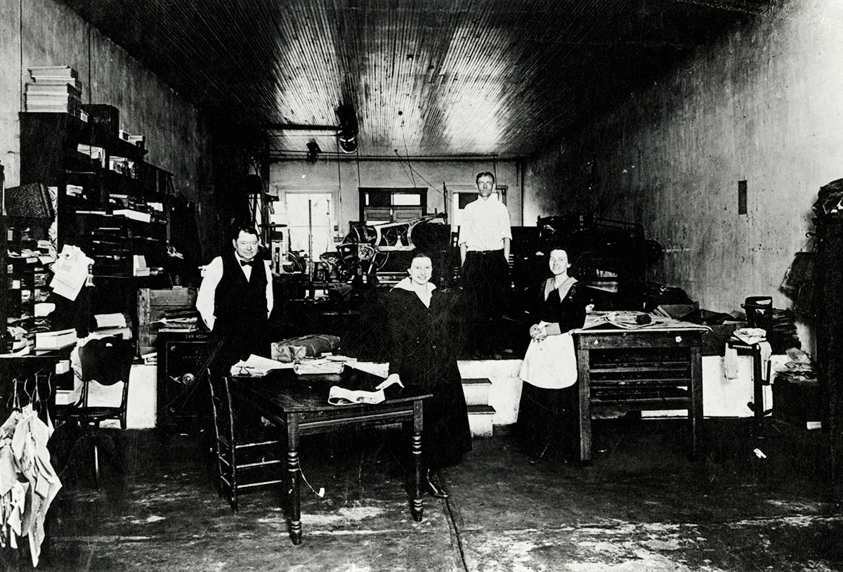 Two white men and two white women in newspaper printing office