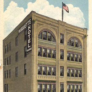 Multistory tan brick building with a sign saying "Marquette Hotel"