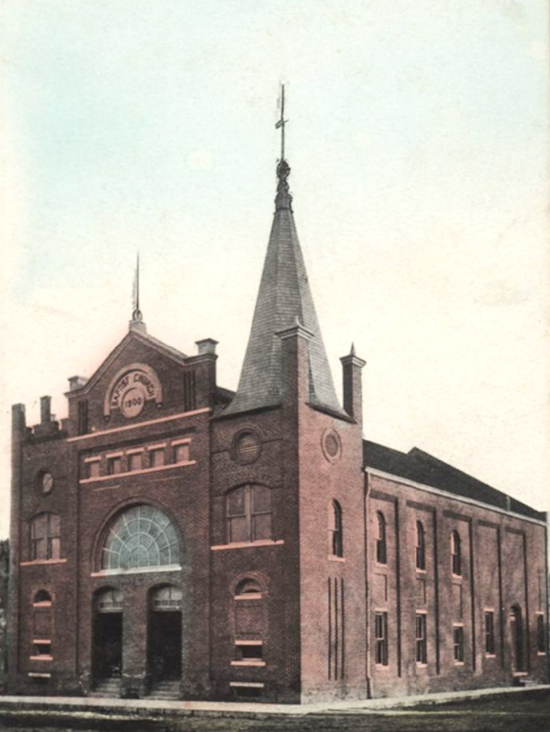 Large brick multistory church building with arched doorways and a spire