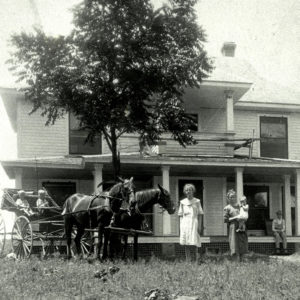 Group of white people on porch and in yard of multistory wooden house