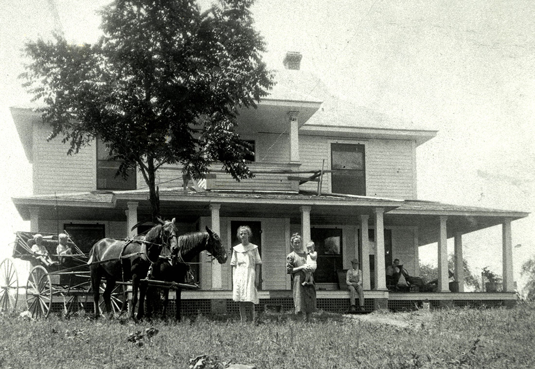 Group of white people on porch and in yard of multistory wooden house