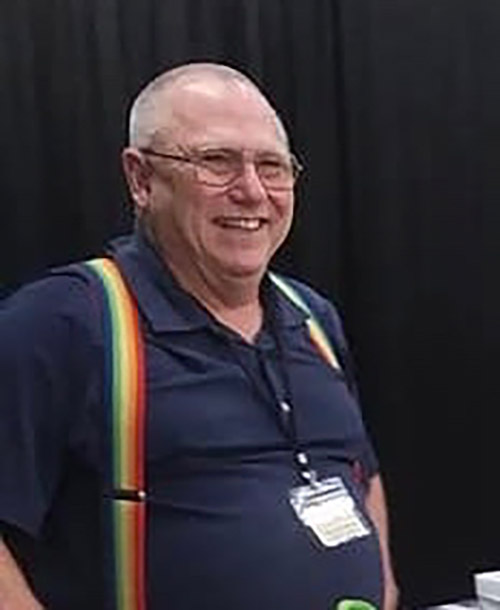 White man in blue short-sleeved shirt and rainbow suspenders