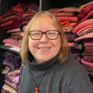 White woman in sweater and necklace. Fabric behind her