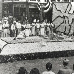 Young white women riding parade float past crowds of people