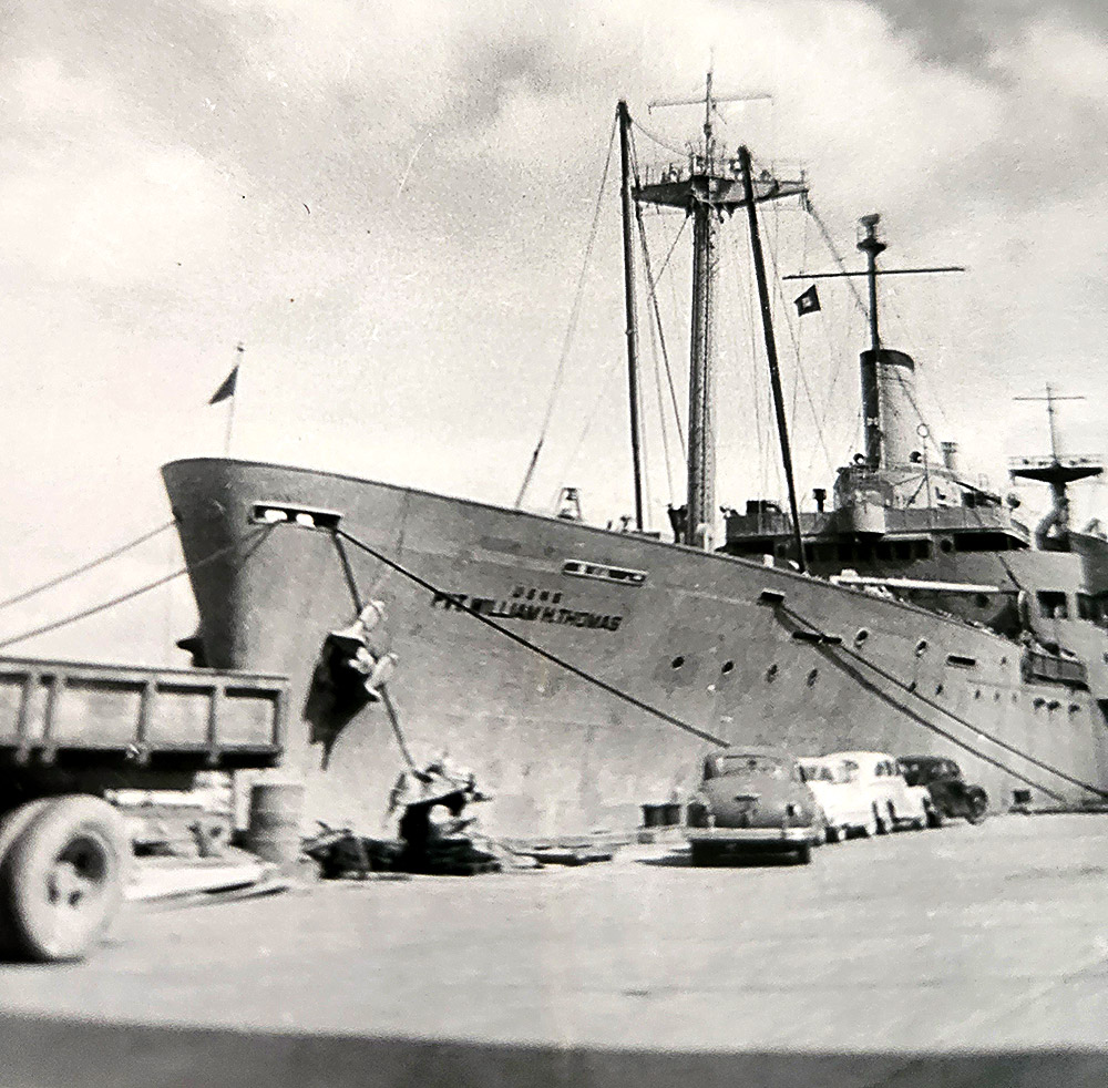 Side view of long ship docked with cars in the foreground