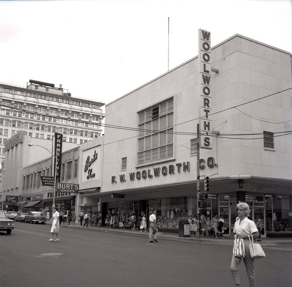 People crossing the street in front of multistory building with a sign saying "Woolworth's"