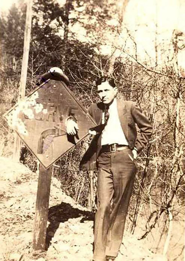 White man in suit and tie posing by road sign saying "curve"