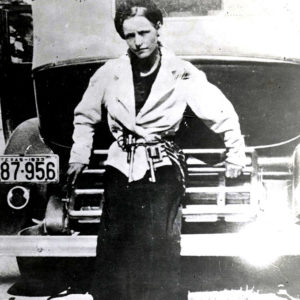 White woman with guns on her belt leaning against car with a 1933 Texas license plate