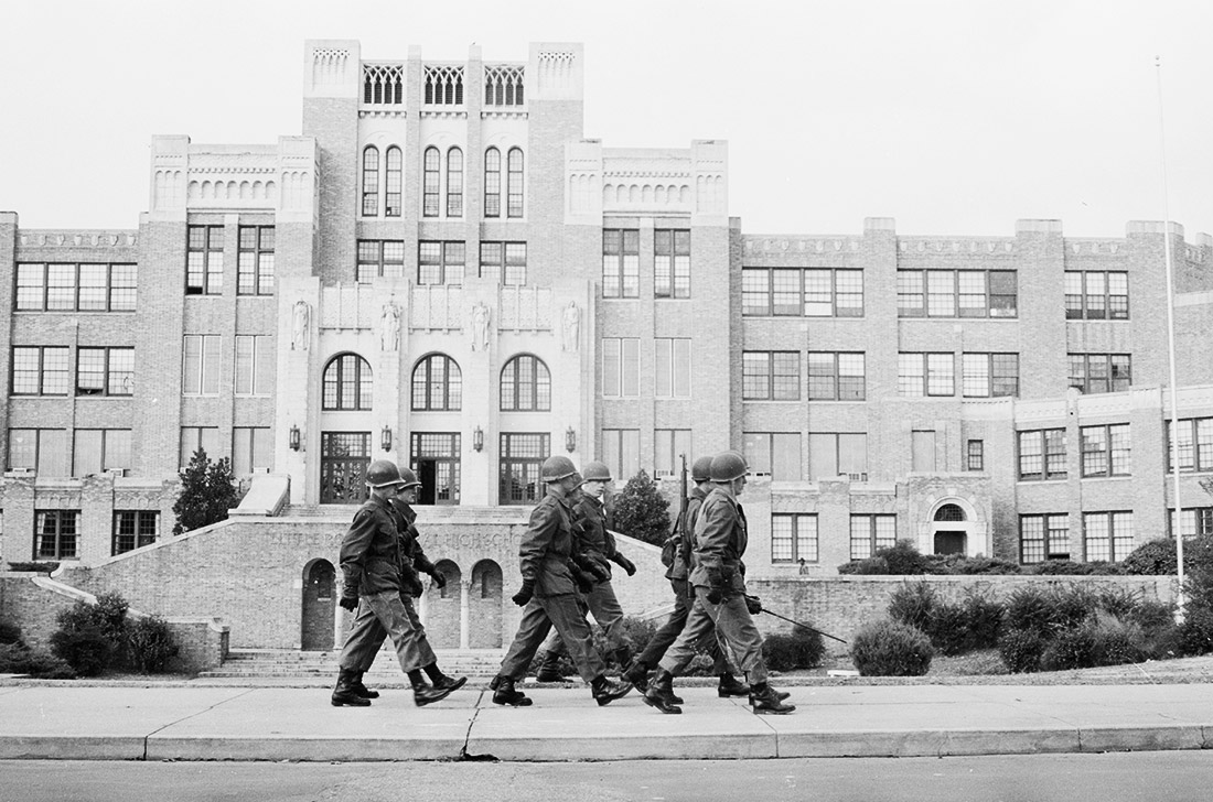 Soldiers in uniform marching in front of multistory school complex