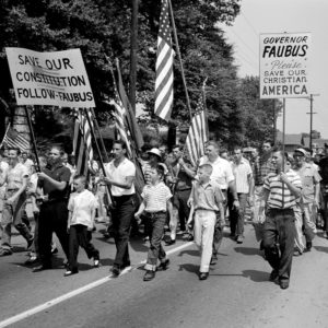 Large group of white men and boys carrying flags and signs supporting Faubus