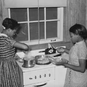 Two African American girls working in kitchen at stove