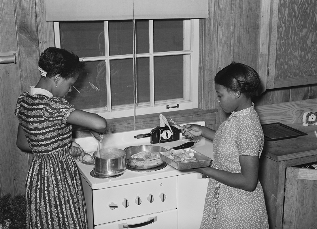 Two African American girls working in kitchen at stove