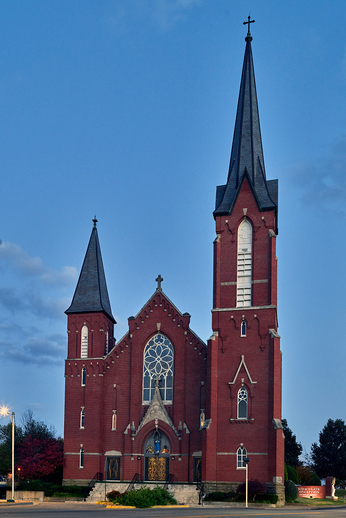 Multistory red brick church building with two spires of different heights
